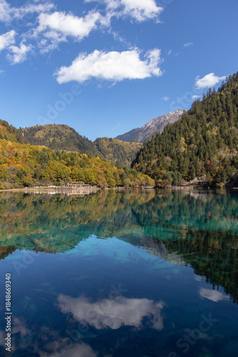 Crystal clear mountain lake reflecting forested slopes and blue sky with white cloud at Five-Flower Lake, Jiuzhaigou in Sichuan, China