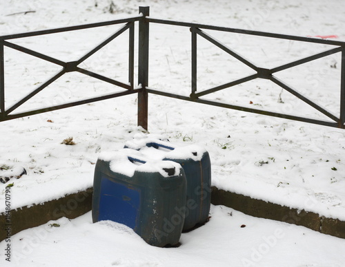 Two canisters are standing near the fence of a snow-covered lawn