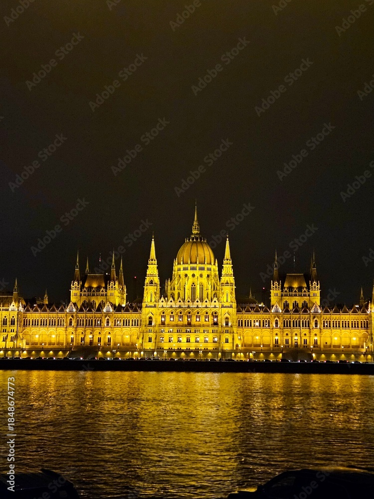 Fototapeta premium Parliament glowing brightly at night in Budapest, Hungary. View across the Danube River.