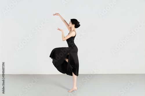 A beautiful girl wearing a black long dress is practicing dance in the dance studio