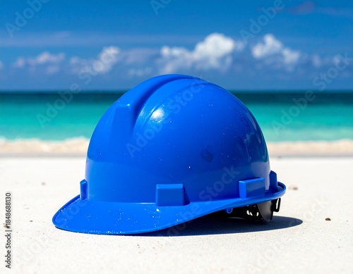 Blue construction helmet resting on white sand beach with ocean view.