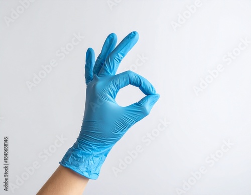 Blue gloved hand making the OK sign against a plain white background, medical concept.