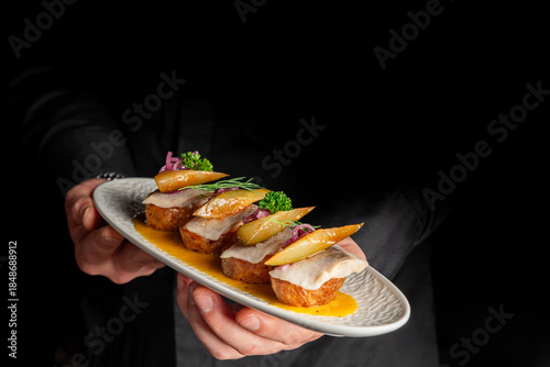 Canvas Print waiter holding a grey oval plate with several pieces of elegant fish canapés or