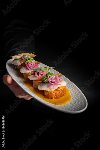 Billede på lærred waiter holding a grey oval plate with several pieces of elegant fish canapés or