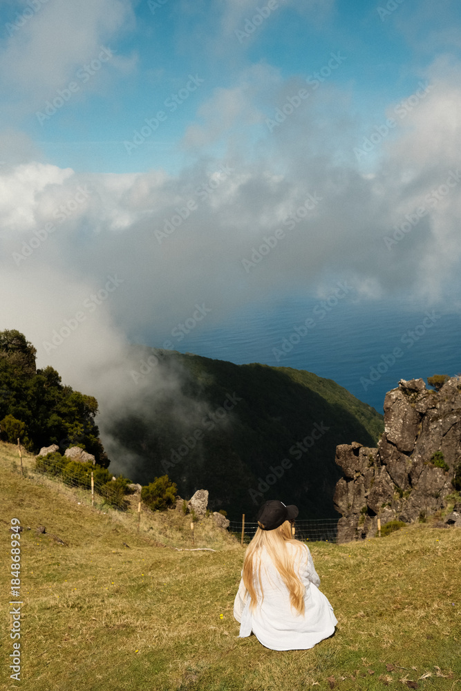 Fototapeta premium Quiet woman seated on cliffside watching foggy bay in solitude