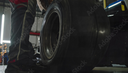 Mechanic Standing Beside Racing Car Tire in Motorsport Pit Garage