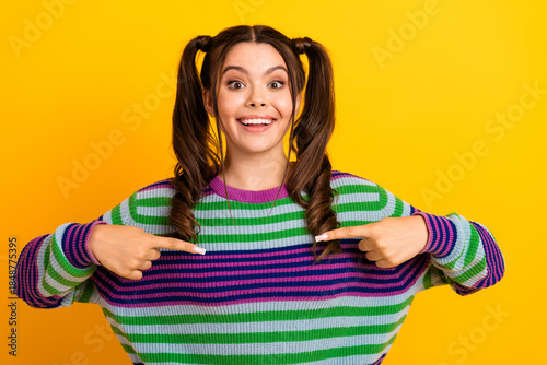 Принти на полотні Young woman with colorful striped sweater smiles and points at herself against a