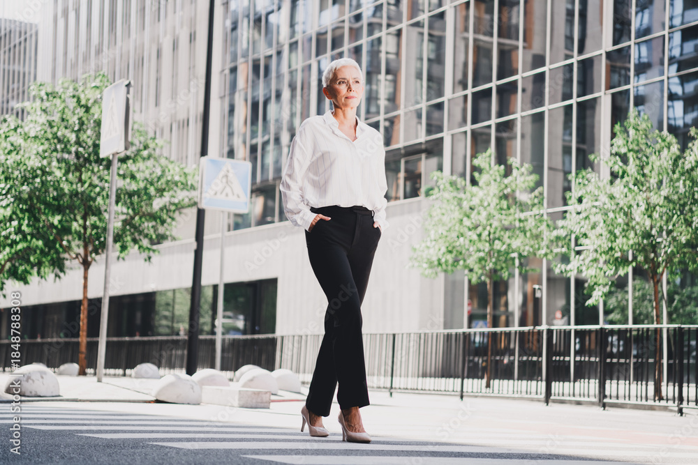 Φωτογραφία Senior businesswoman walking in a megacity street scene beside modern office bui
