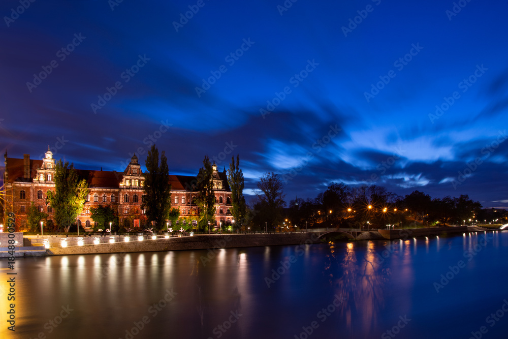 Fototapeta premium Night Riverside Cityscape With Historic Building And Water Reflections. Long Exposure Blue Hour Cityscape.