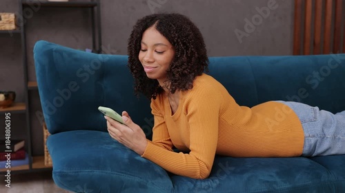 Little kid teen girl wear casual clothes hold in hand use mobile cell phone lay down on blue sofa couch stay at home hotel flat rest relax spend free spare time in living room indoor. Lounge concept