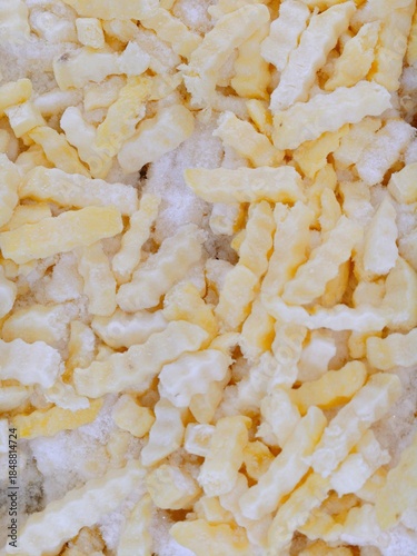 Full-Frame Background of Frozen, Uncooked Crinkle-Cut French Fries or Potato Sticks on Ice