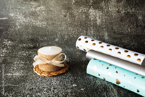 Wallpaper Mural White decorative candle with bow and rolls of gift wrapping paper on dark textured background. Cozy minimal holiday setting, perfect for gifting, celebration, or DIY packaging themes Torontodigital.ca
