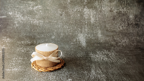 Wallpaper Mural White candle wrapped in rustic burlap and decorated with beige ribbon, placed on woven mat over dark textured background. Minimalist cozy decor for holidays, gift or relaxation Torontodigital.ca