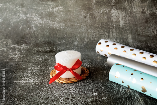 Wallpaper Mural White decorative candle with bow and rolls of gift wrapping paper on dark textured background. Cozy minimal holiday setting, perfect for gifting, celebration, or DIY packaging themes Torontodigital.ca