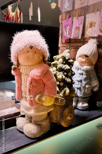 Holiday decor with dolls in winter outfits, Christmas tree, and sleigh at flower shop. Christmas holiday concept. Vertical
