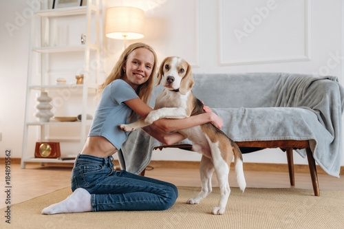 Smiling, having fun. Girl is with her dog on the floor in a cozy living room