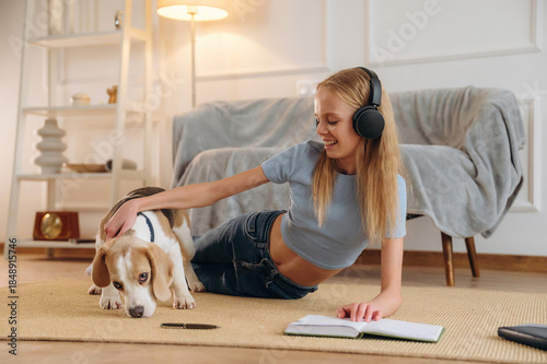 In headphones, listens to the music, with animal. Happy girl is on the floor at home with dog, domestic room
