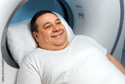 A middle-aged man with a stocky build lies on a table inside an MRI machine, looking happy and smiling.