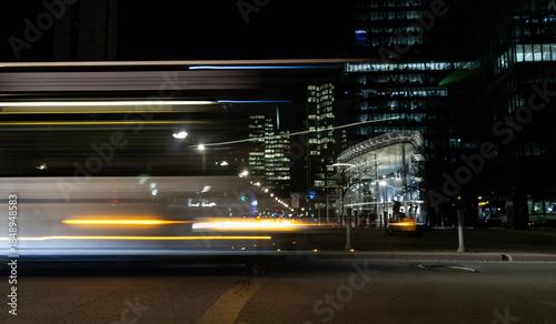 Fotografija Dynamic motion blur of a bus passing modern glass office buildings at night in the business district of Brussels, Belgium