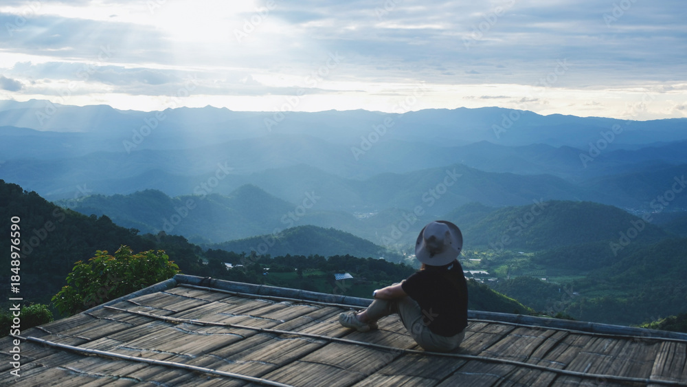Naklejka premium Rear view of a woman sitting on wooden terrace and looking at a mountain view before sunset