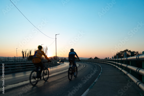 Obraz na płótnie Two Cyclists Crossing an Asphalt Overpass at Dramatic Sunset