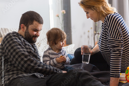 Young family relaxing in bed, mother drinking water