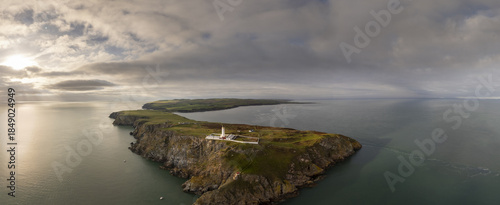 Aerial view of Mull of Galloway Lighthouse standing tall against the rugged coastline, where the land meets the sea under a sky of moody clouds, Stranraer, Scotland, United Kingdom.