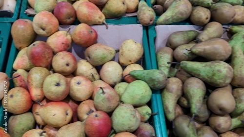 Fruit market displays various types of pears and apples in bright colors during mid-morning hours in a busy shopping area
