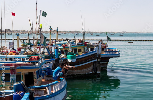 View of vibrant fishing boats bobbing gently in the turquoise water, adorned with Pakistani flags, under a clear sky, Gwadar, Balochistan, Pakistan.