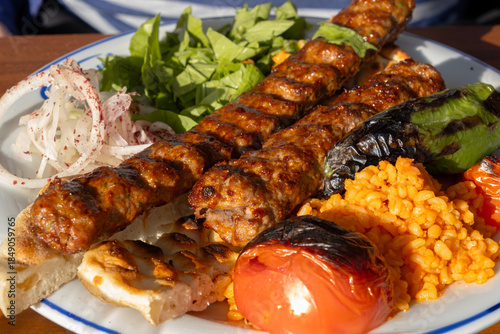 Fotografia Adana kebab plate with two juicy grilled meat skewers, bulgur pilaf, charred pep