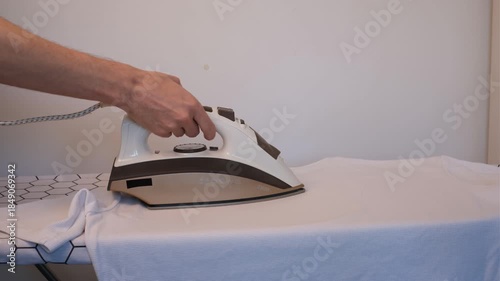 Man ironing a white t-shirt with a steam iron on a white background, close-up of hands