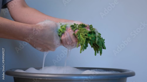 Woman wringing out a floor cleaning rag in a basin with foam on a white background, close-up of hands