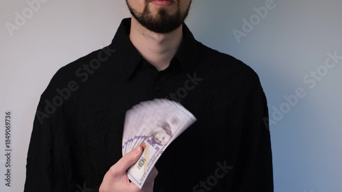 Young man in black formal shirt fans himself with one hundred dollar bills on white background