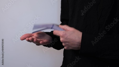 Young man in black shirt handling a stack of banknotes in his hands on white background close-up of hands