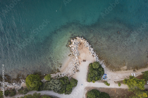 Aerial view of the tranquil turquoise waters meeting the rocky coastline, fringed by verdant trees and pathways, Rovinj, Istria County, Croatia.