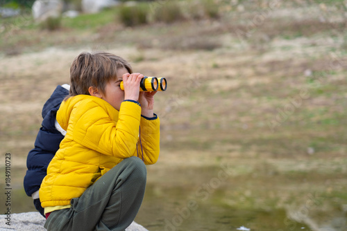 Curious child exploring nature with binoculars by the river