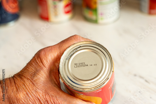 Hand holding canned food showing expired use by date on base before consumption decision