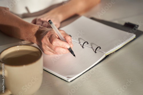 Tableau sur toile Caucasian mature female hand writing in notebook at table with coffee during quiet selfcare planning moment