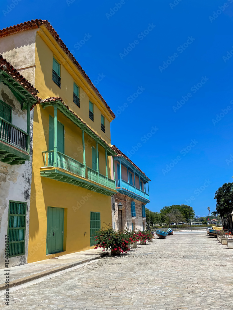 Fototapeta premium Vibrant colors colonial buildings with balconies in Old Havana, Cuba. Cobblestone streets and clear blue sky