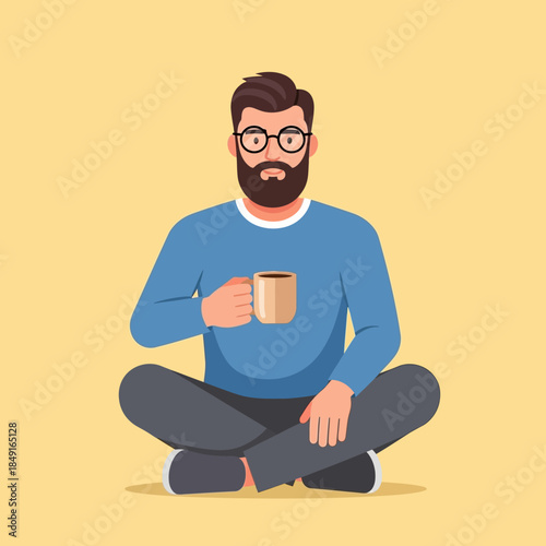 Bearded man with glasses sitting cross-legged on the floor, holding a coffee mug, against a plain yellow background.