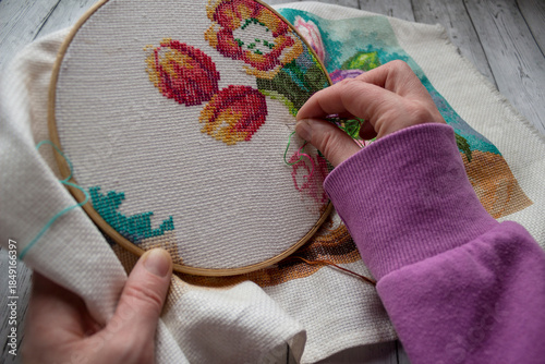 Fotografie Woman’s hands embroidering colorful flowers using cross-stitch technique on fabric