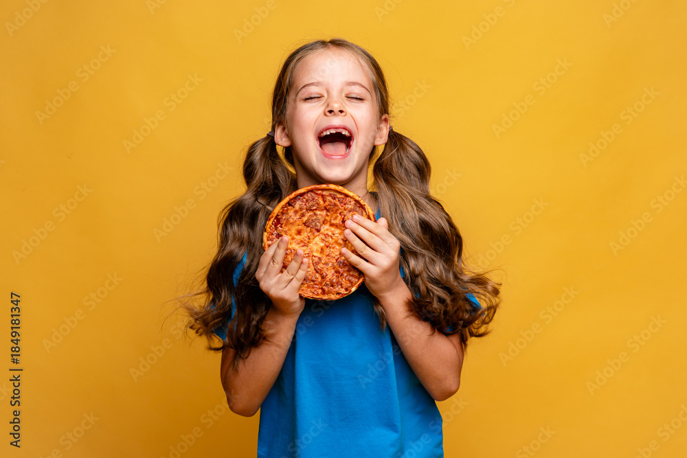 Φωτογραφία Hungry little girl in blue t-shirt holds tasty junk food pizza on yellow background, closed eyes from pleasure