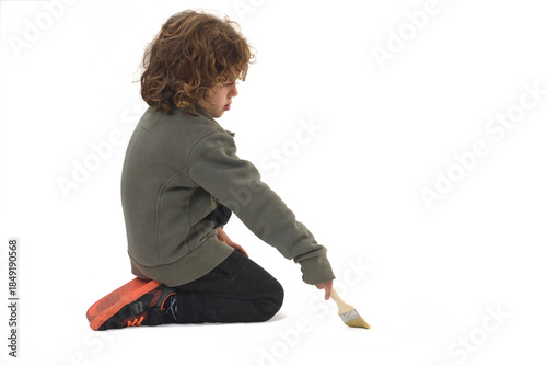 side view of a kneeling child painting with a brush on white background