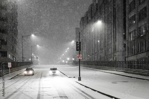 View of a snow-covered street scene with cars moving along the road under the glow of streetlights during a heavy snowfall, Washington DC, United States.
