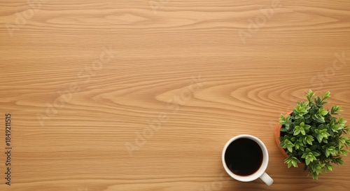 Overhead view of a white coffee mug and a potted plant on a wooden desk