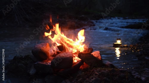 Night cozy campfire and beautiful mountain river in light of flashlight. Calm bonfire, burning old wood in spring time. Active lifestyle, traveling, hiking. Camping vibes and outdoor lifestyle mood