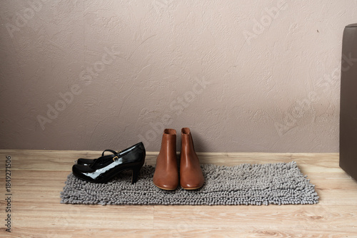 Brown ankle boots and black shoes on rug in entryway