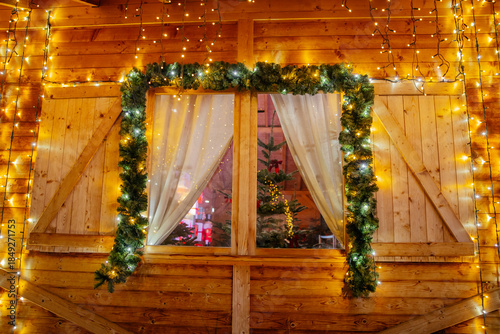 Wooden cottage window with Christmas lights and decorations and trees inside. 