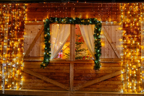Wooden cottage window with Christmas lights and decorations and trees inside. 