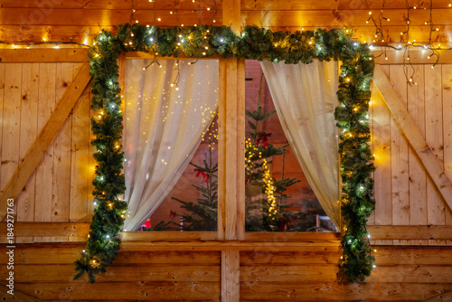 Wooden cottage window with Christmas lights and decorations and trees inside. 
